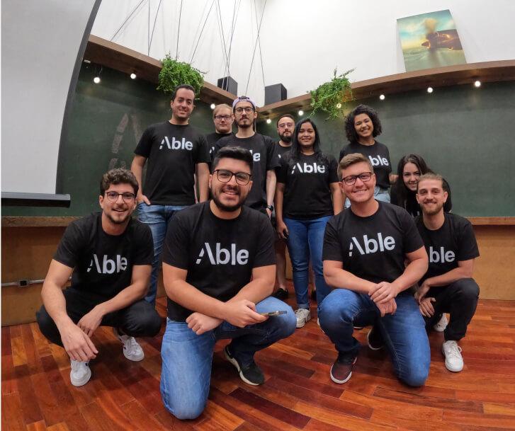 Indoor team photo of 11 members of the Able team in matching black Able company tshirts