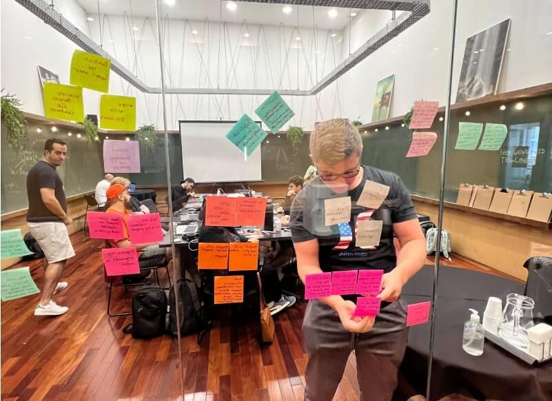 Photo of a young man at Able in a team meeting contributing ideas by adding notes to a glass conference room wall